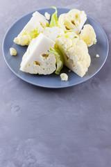 Cauliflower on a gray plate. Sliced fresh cauliflower on a cement background. Slices of organic cabbage on a plate. Top view. Copy space