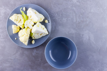 Cauliflower on a gray plate. Sliced fresh cauliflower on a cement background. Slices of organic cabbage on a plate. Top view. Copy space