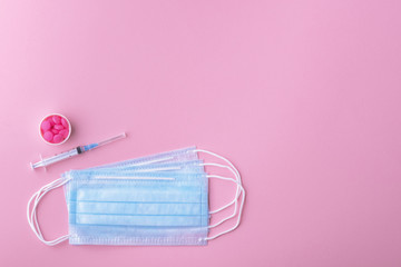 Medical mask surgical protective virus, flu, disease, pills and syringe. Isolated on a pink background.