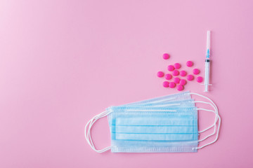 Medical mask surgical protective virus, flu, disease, pills and syringe. Isolated on a pink background.
