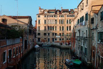 Venice, Italy - February 19 2020 : Water reflections on canal and in the background people enjoy the sunny day
