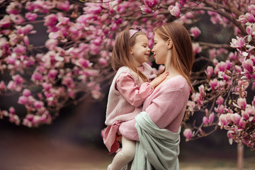 Happy family mother and daughter in pink clothes in the spring in a flowered park for a walk. a...