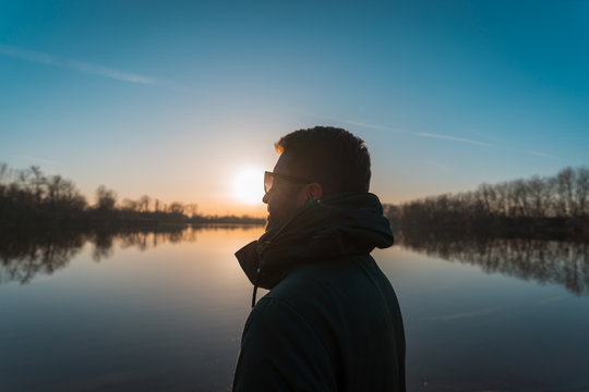 Guy with sunglasses looking at the distance with sunset and lake in the background