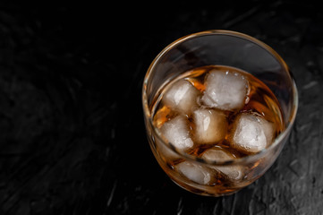 
glass of whiskey with ice on a black stone background with copy space for your text.
