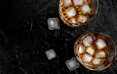 Two glasses of whiskey with ice on a black stone background with copy space for your text.