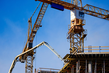 Fototapeta na wymiar Construction site close up. Crane against blue sky background. Yellow hoisting cranes with cabins. Industrial construction. Copy space 