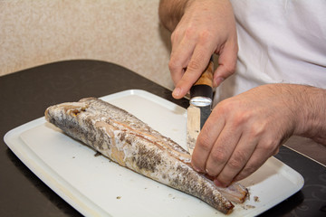 A man in a white t-shirt cuts up fish. Black bread made from coarse flour and green onions. Still life on the kitchen Board. Hearty food for cold regions.