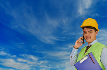 Young engineer with helmet  and clipboard, speaking on mobile phone