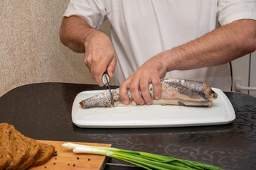 A man in a white t-shirt cuts up fish. Black bread made from coarse flour and green onions. Still life on the kitchen Board. Hearty food for cold regions.