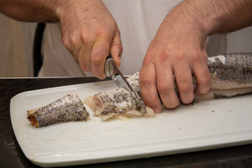 A man in a white t-shirt cuts up fish. Black bread made from coarse flour and green onions. Still life on the kitchen Board. Hearty food for cold regions.
