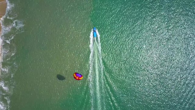 Aerial footage of parasailing kiting activity: people towed behind a boat while attached to a specially designed canopy wing that resembles a parachute, at the Malaysian coast - tourist attraction.