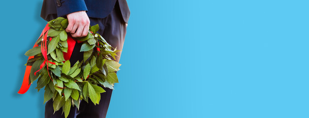 Corona di Alloro per un laureato tenuta in mano. Sfondo panoramico di colore blu. Banner.