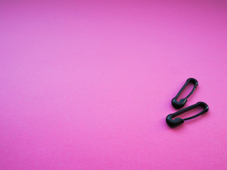 two black closed safety pins on a bright pink background