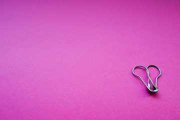 Two gray closed safety pins on a bright pink background are stacked on top of each other . Items for sewing and decoration