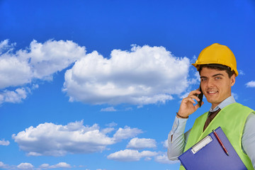 Young engineer with helmet  and clipboard, speaking on mobile phone