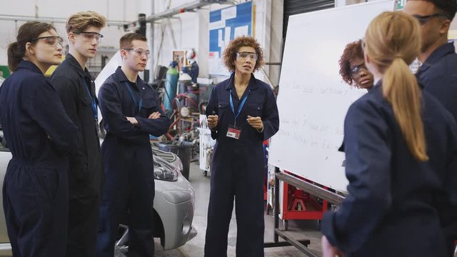 Students studying for auto mechanic apprenticeship at college raising hand and asking female tutor question - shot in slow motion