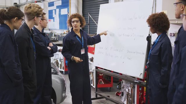 Female tutor by whiteboard with students teaching auto mechanic apprenticeship at college - shot in slow motion