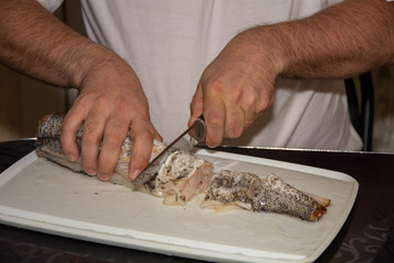 A man in a white t-shirt cuts up fish. Black bread made from coarse flour and green onions. Still life on the kitchen Board. Hearty food for cold regions.