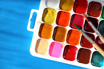 Set of watercolor paints with dirty brushes on blue background. Shooting with hard shadows.