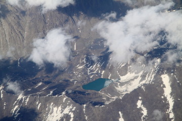 Scenic mountains view from the plane. Beautiful top landscape. Mountains surrounded by clouds. Ice and small lake into mountains. Wallpaper and background.