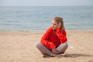Fototapeta na wymiar Beautiful blonde woman sits on a sandy beach alone