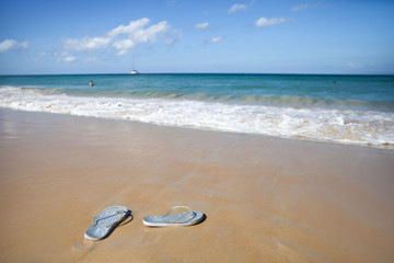 Fototapeta na wymiar Silver flip flops on a sandy beach