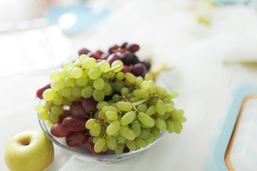 Multicolored grapes in a beautiful plate on a light background.