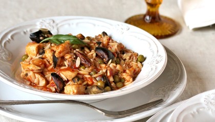 paella from orzo pasta with mussels, seashells and chicken. Seafood paella, traditional spanish dish. Paella on rustic black wooden table. Top view