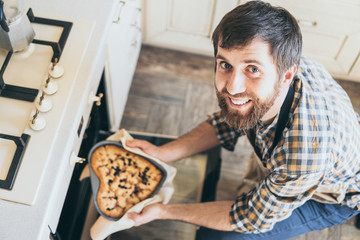 Bearded young man taking heart shaped cake out of the oven