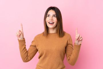 Young woman over isolated pink background surprised and pointing up