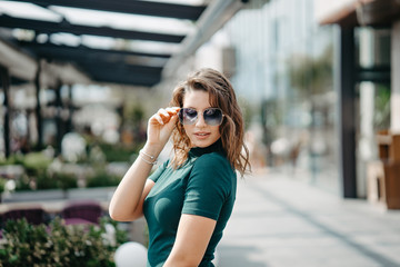 A beautiful young brunette girl is walking in the city in sunglasses and posing for the camera