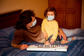 father and daughter, in medical masks, sit at home in quarantine, because of the covid-19 pandemic, and learn to play the piano