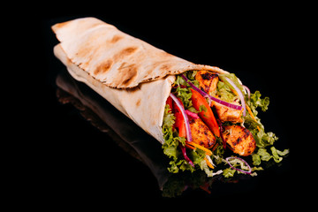Delicious turkish doner kebab with chicken grilled, onion, tomatoes, lettuce, parsley, carrot,  cucumbers and sauce isolated on black background 