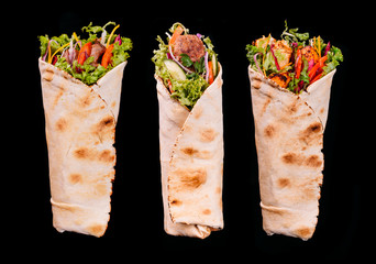 Delicious turkish doner kebab with chicken,lamb,beef grilled, onion, tomatoes, lettuce, parsley, carrot,  cucumbers and sauce isolated on black background 