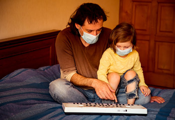 Fototapeta na wymiar father and daughter, in medical masks, sit at home in quarantine, because of the covid-19 pandemic, and learn to play the piano