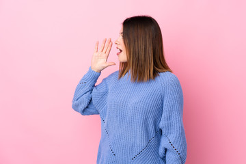 Young woman with blue sweater over isolated pink background shouting with mouth wide open