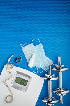 Sport equipment, scales, medical masks and sanitizer on blue background. Fitness. Weight and health control during quarantine.