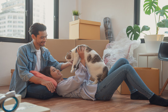 Young Asian couple or family feeling happy relaxing and play with their cat after moving to new house or apartment.