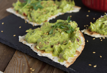 fresh guacamole sauce with peas microgreen and sesame seeds on toasted tortillas on a black slate plate