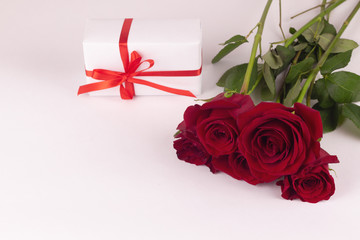 A bouquet of red roses and a gift with a ribbon lie on a white background.