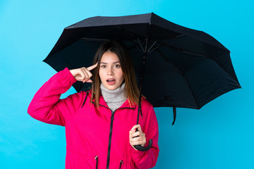 Young woman holding an umbrella over isolated blue wall intending to realizes the solution