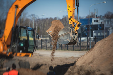 Yellow heavy excavator excavating sand and working during road works, unloading sand during...