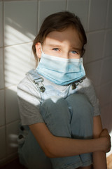 Little sad girl is sitting at the kitchen during sunny day on white tiles background wearing a...