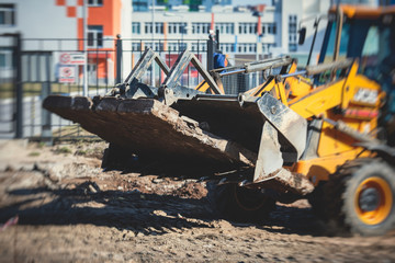 Yellow heavy excavator excavating sand and working during road works, unloading sand during construction of the new road with workers around