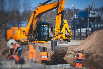 Yellow heavy excavator excavating sand and working during road works, unloading sand during construction of the new road with workers around