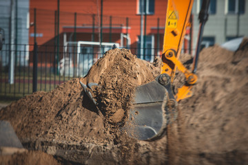 Yellow heavy excavator excavating sand and working during road works, unloading sand during construction of the new road with workers around