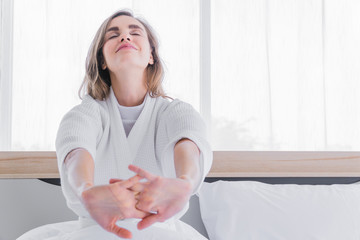 Woman waking up from the bed and stretching her hands.