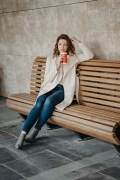 Beautiful young girl sitting and enjoing coffee .sitting on a bench in the city