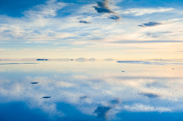 Mirror surface of Salar de Uyuni salt flat at sunset in Bolivia. Clouds and sky and their...