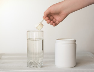 hand holding scoop of fish collagen. collagen peptides in container or jar. glass of water for mixing drink. Healthcare supplement concept. collagen powder for skin and joints .